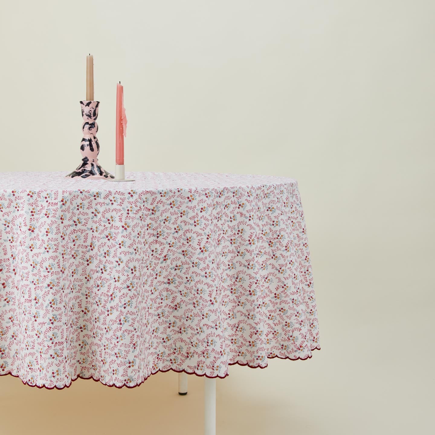 Round little flowers tablecloth in maroon on table with candles in candleholders.