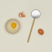 Simple metal flat slotted spoon in brass with cracked egg in bowl and egg shells.