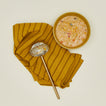Simple metal ladle in brass with kitchen towel and a bowl of soup