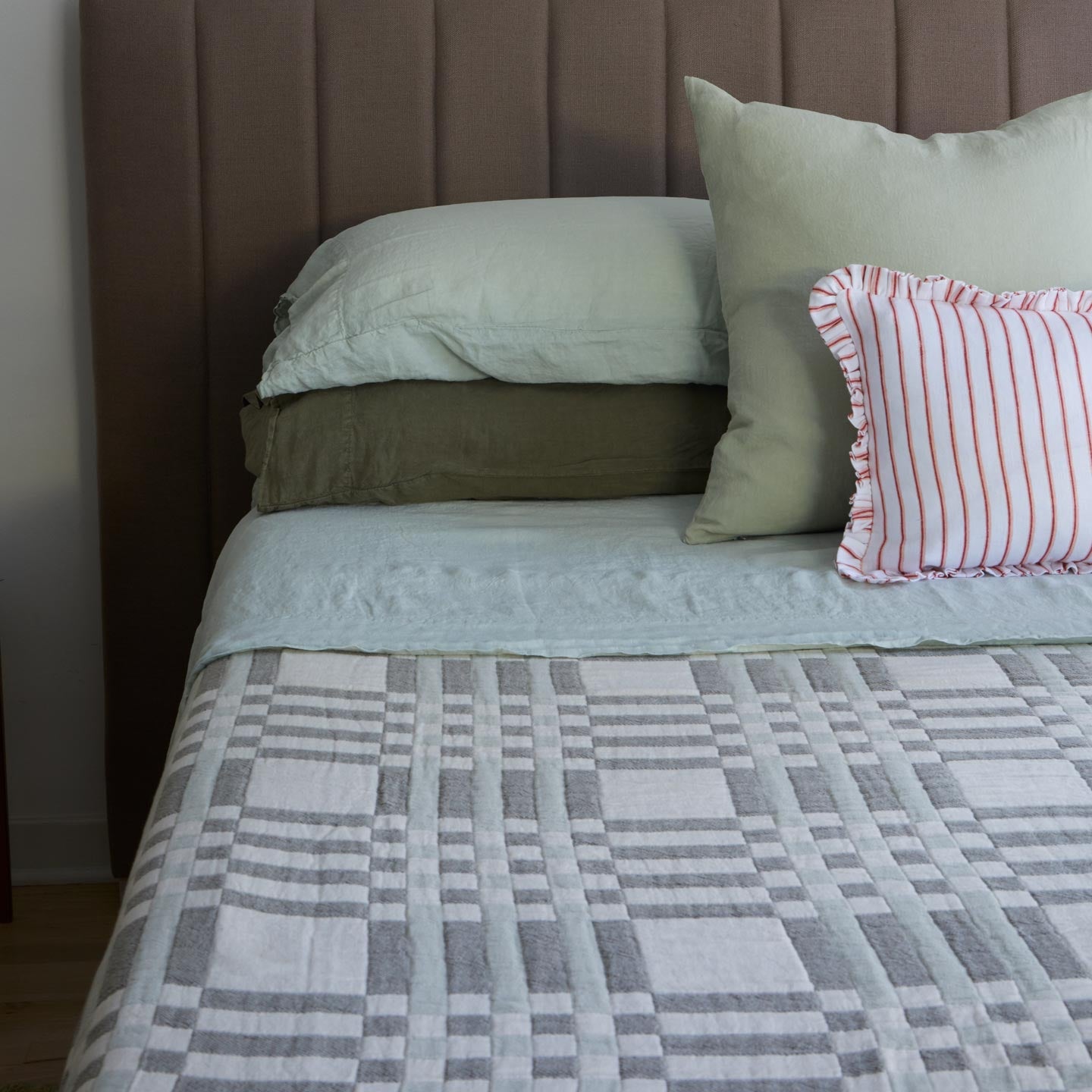 Bed with green bedding and a striped pillow against a brown headboard.