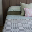 Bed with green bedding and a striped pillow against a brown headboard.