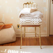 Stack of blankets on a gold chair against a beige wall with decorative patterns.