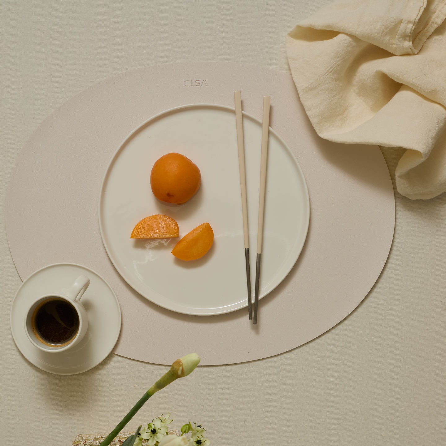Table setting with a plate of fruit, coffee, and chopsticks on a beige surface.