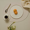 Café setting with a cup of coffee, plate with pastries, and spoon on a beige surface.
