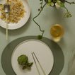 Table setting with a plate of artichoke, a glass of white wine, and a bowl of rice with a spoon.