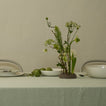 Table setting with a vase of greenery and white flowers on a light green tablecloth.