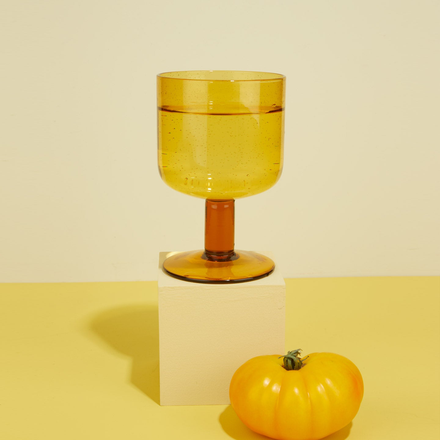 Amber Simple Seeded Glass on cube with pepper on yellow background.