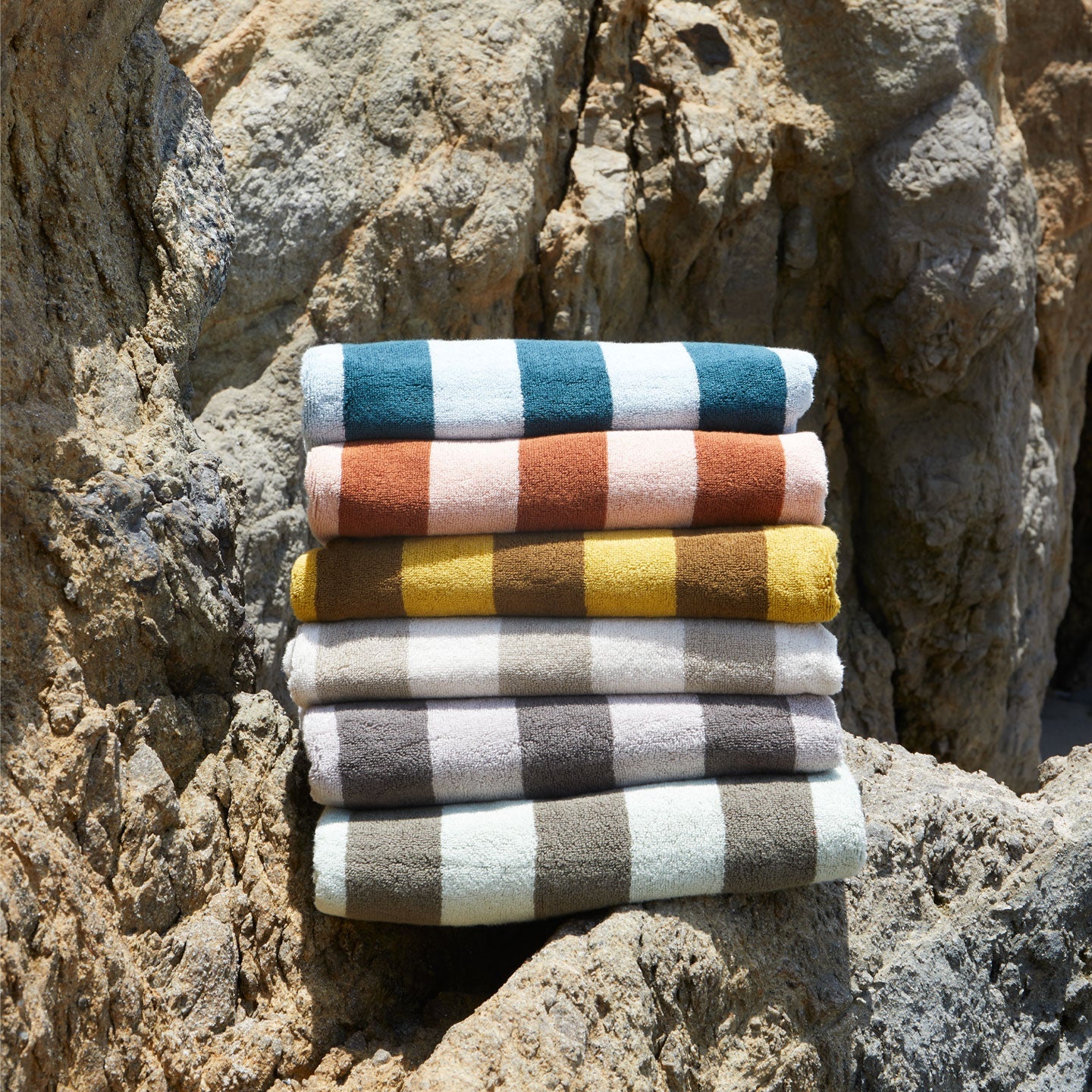 	A stack of striped terry towels in six colors on a rock formation.