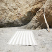 A striped ivory and flax terry towel at the beach.