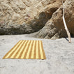 	A striped mustard and bronze terry bath towel at the beach.