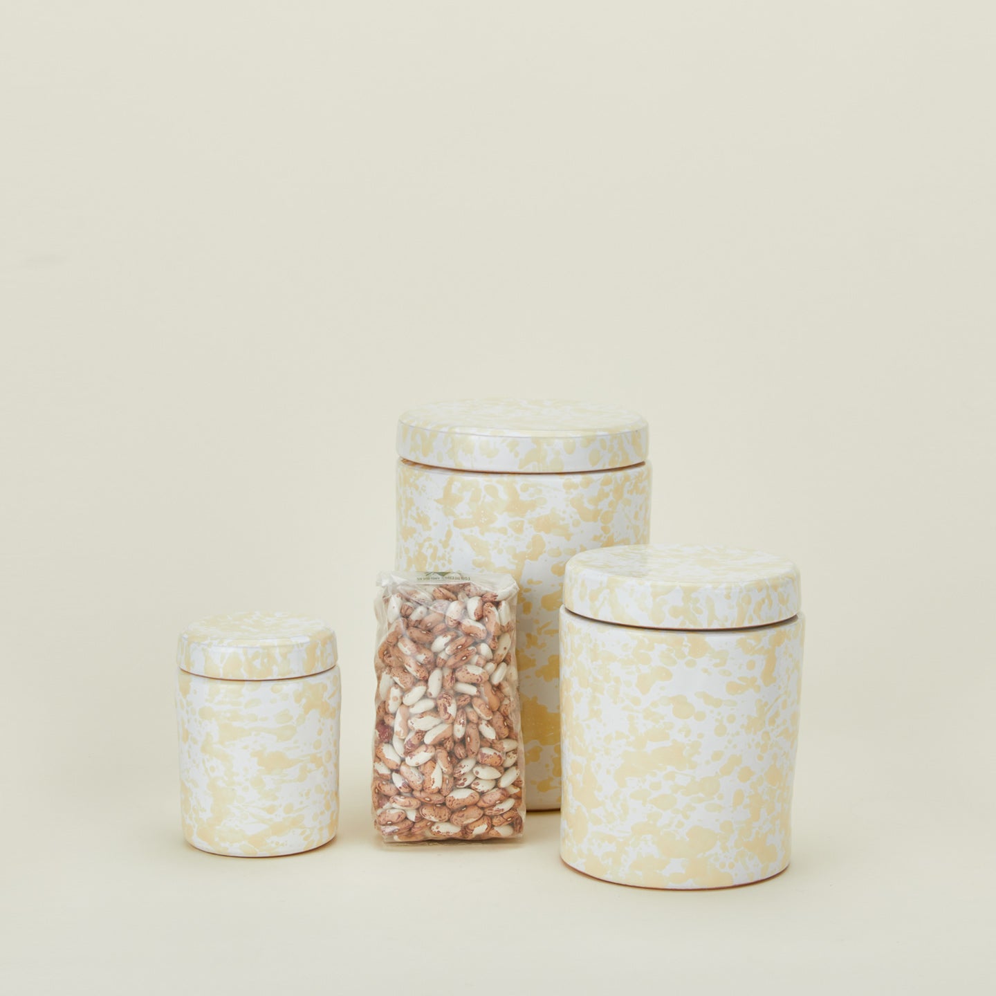 Large, medium, and small splatterware canisters in white and ivory with beans