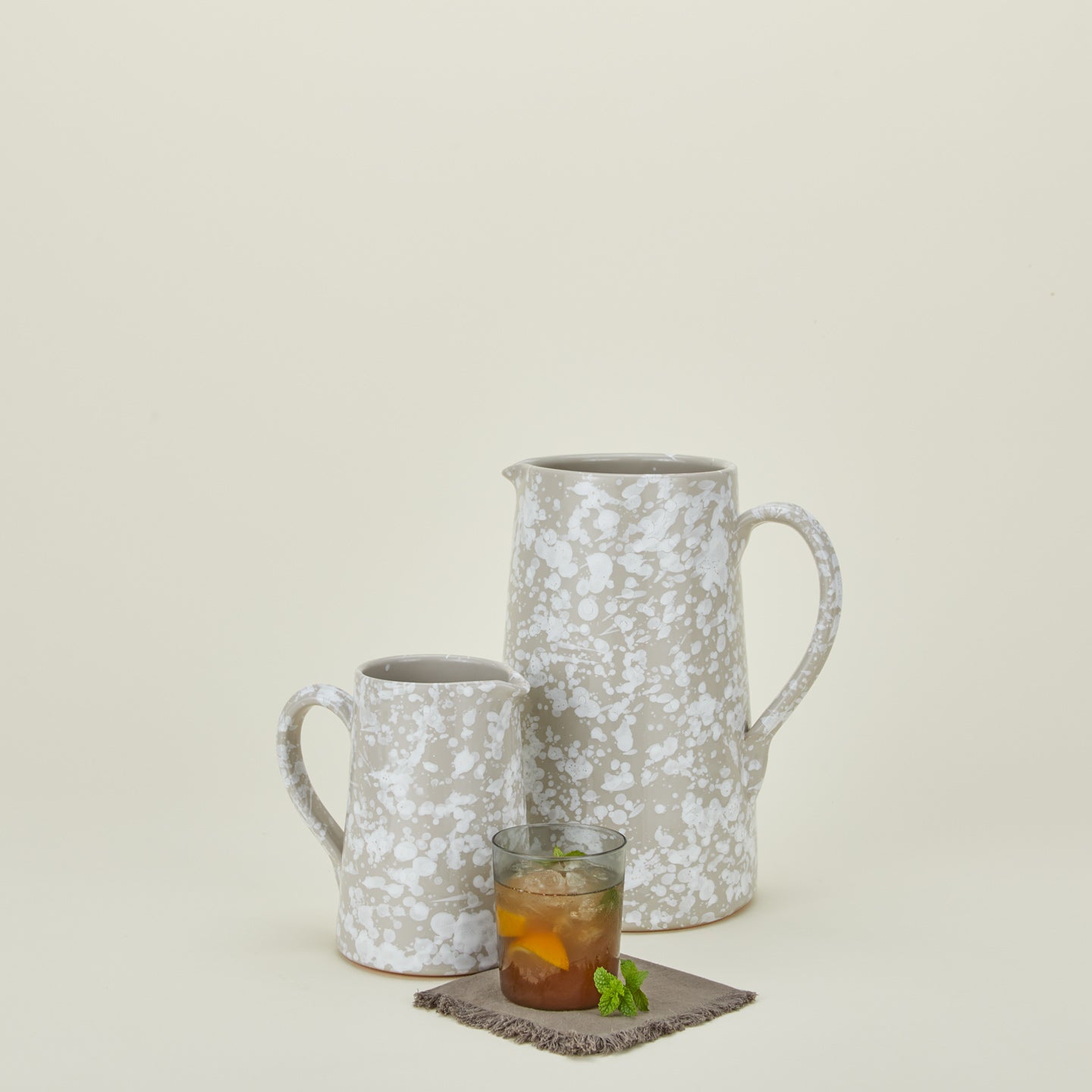 Large and small splatterware pitchers in grey and white with glass on a cocktail napkin