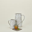 Large and small splatterware pitchers in grey and white with glass on a cocktail napkin