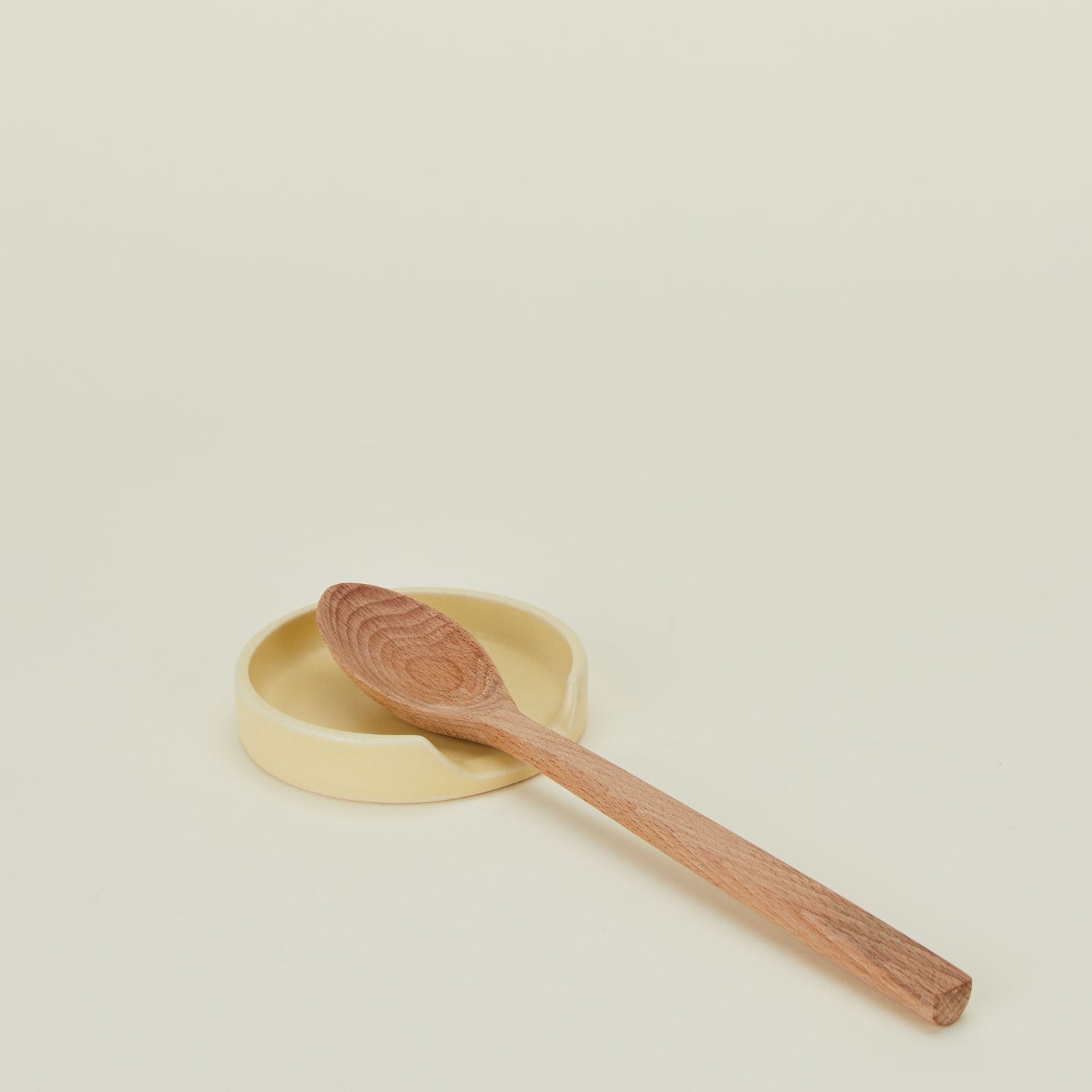 A butter stoneware spoon rest with a wooden spoon.